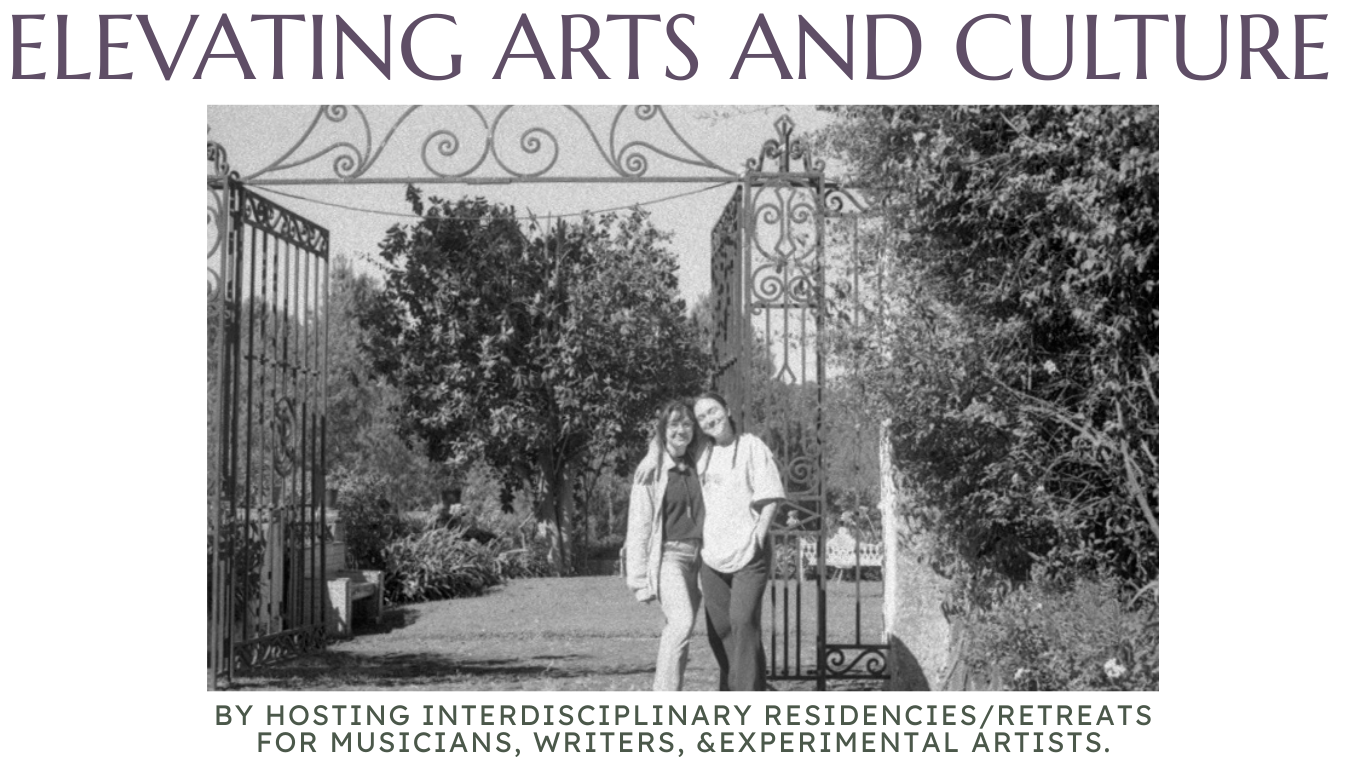 Untitled black and white image of two femme artists by an iron fence with swirling flourishes with large trees behind them
